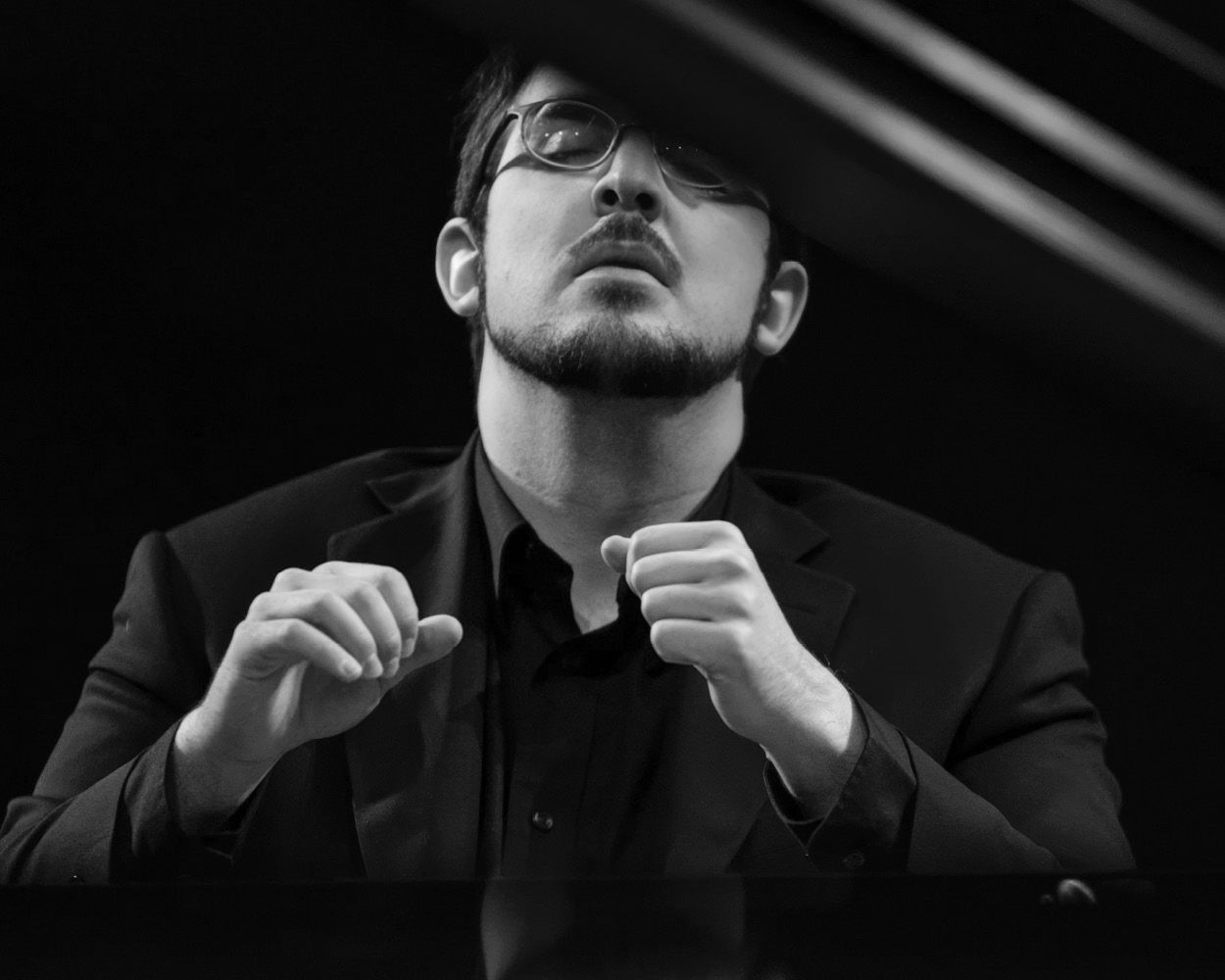 A man in a suit and glasses is playing a piano.