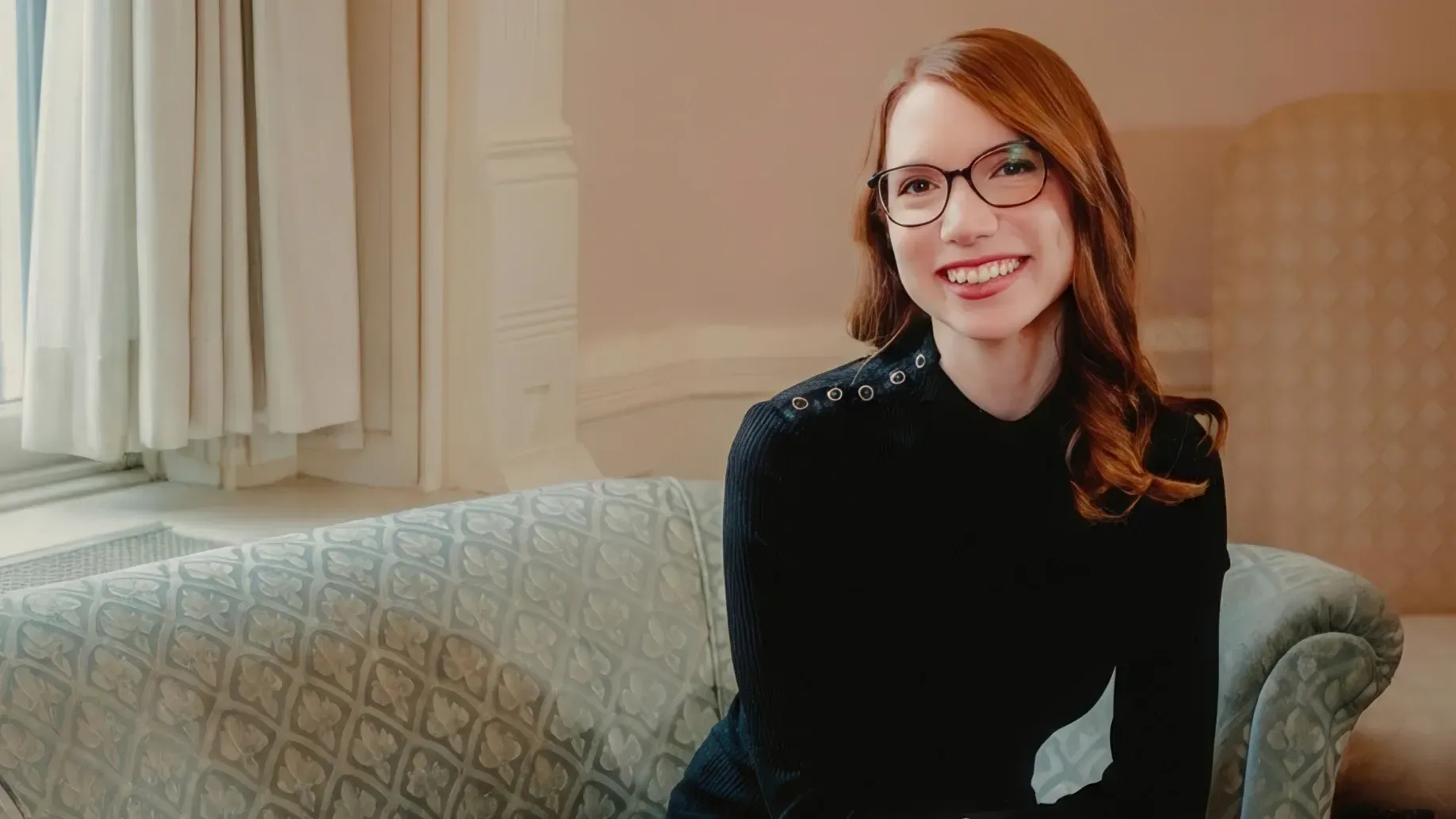 A woman in a black sweater sitting on a sofa.