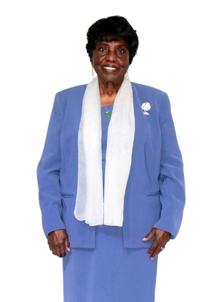 Person in blue suit and white scarf, smiling, standing in front of white background.