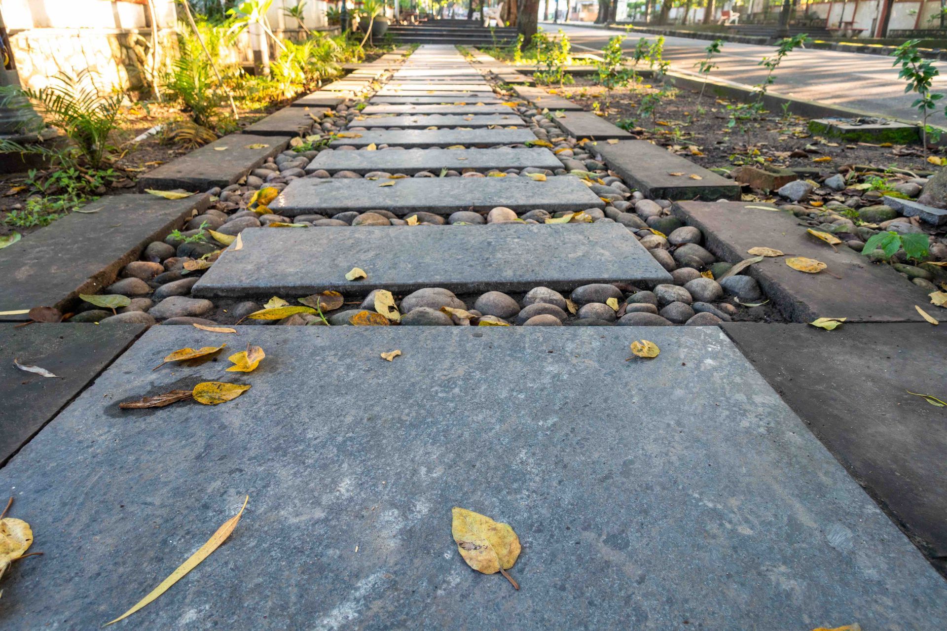 A stone walkway in a park with leaves on the ground