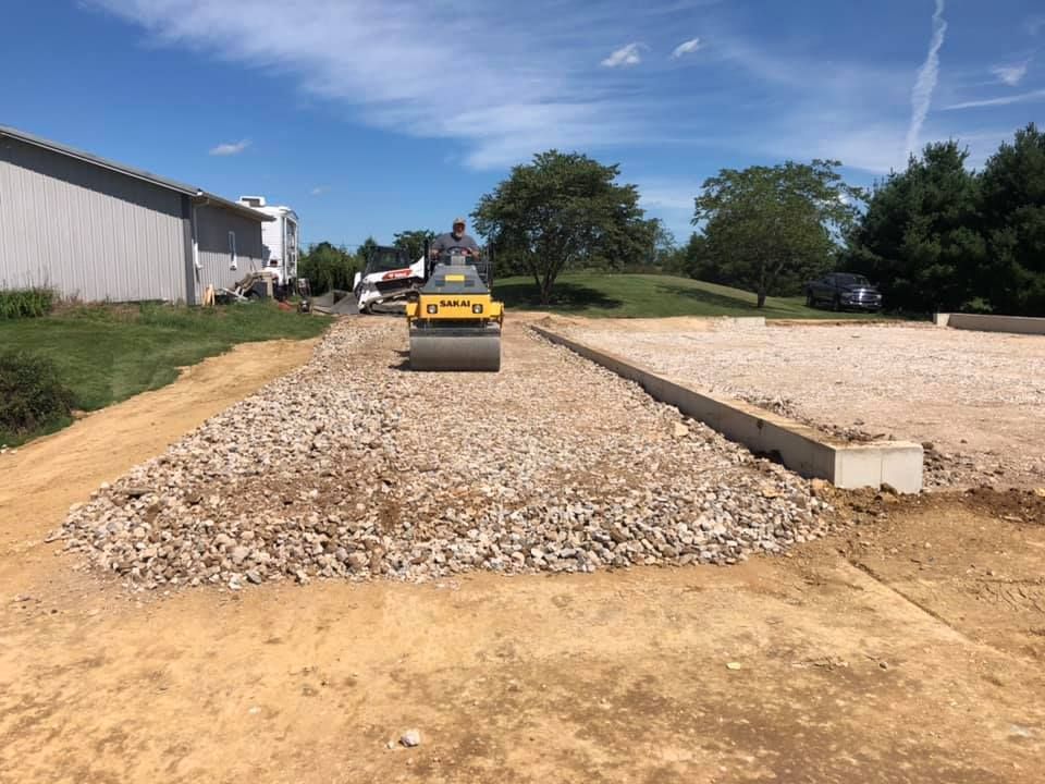 A man is driving a yellow roller on a gravel road.