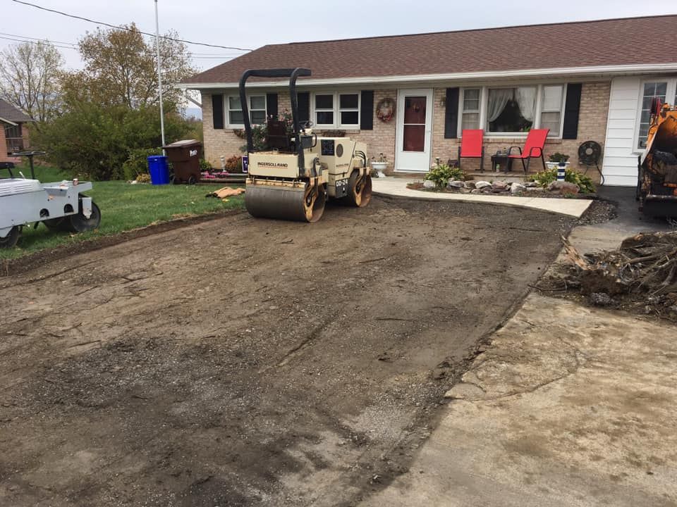 A road roller is working on a driveway in front of a house.