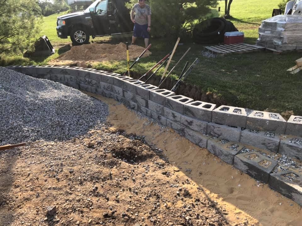 A man is digging a hole in the ground next to a brick wall.