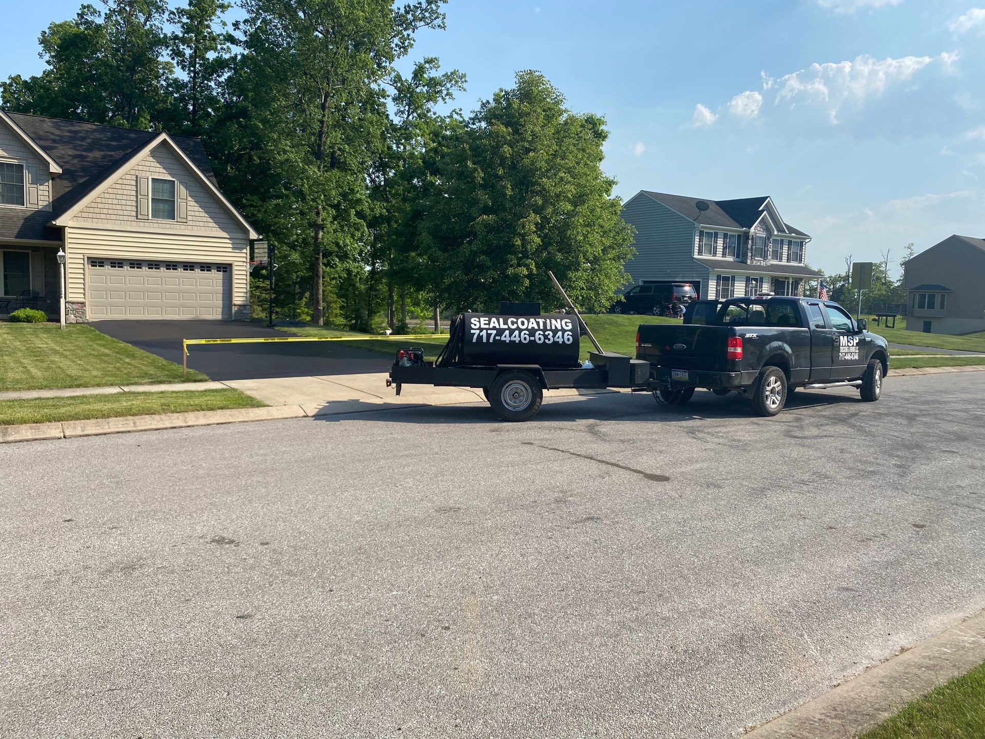 A truck is towing a trailer down a street in front of a house.