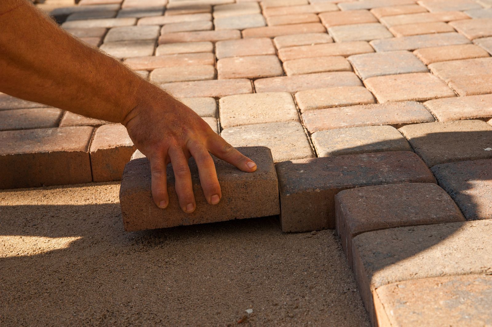A person is laying bricks on a sidewalk.