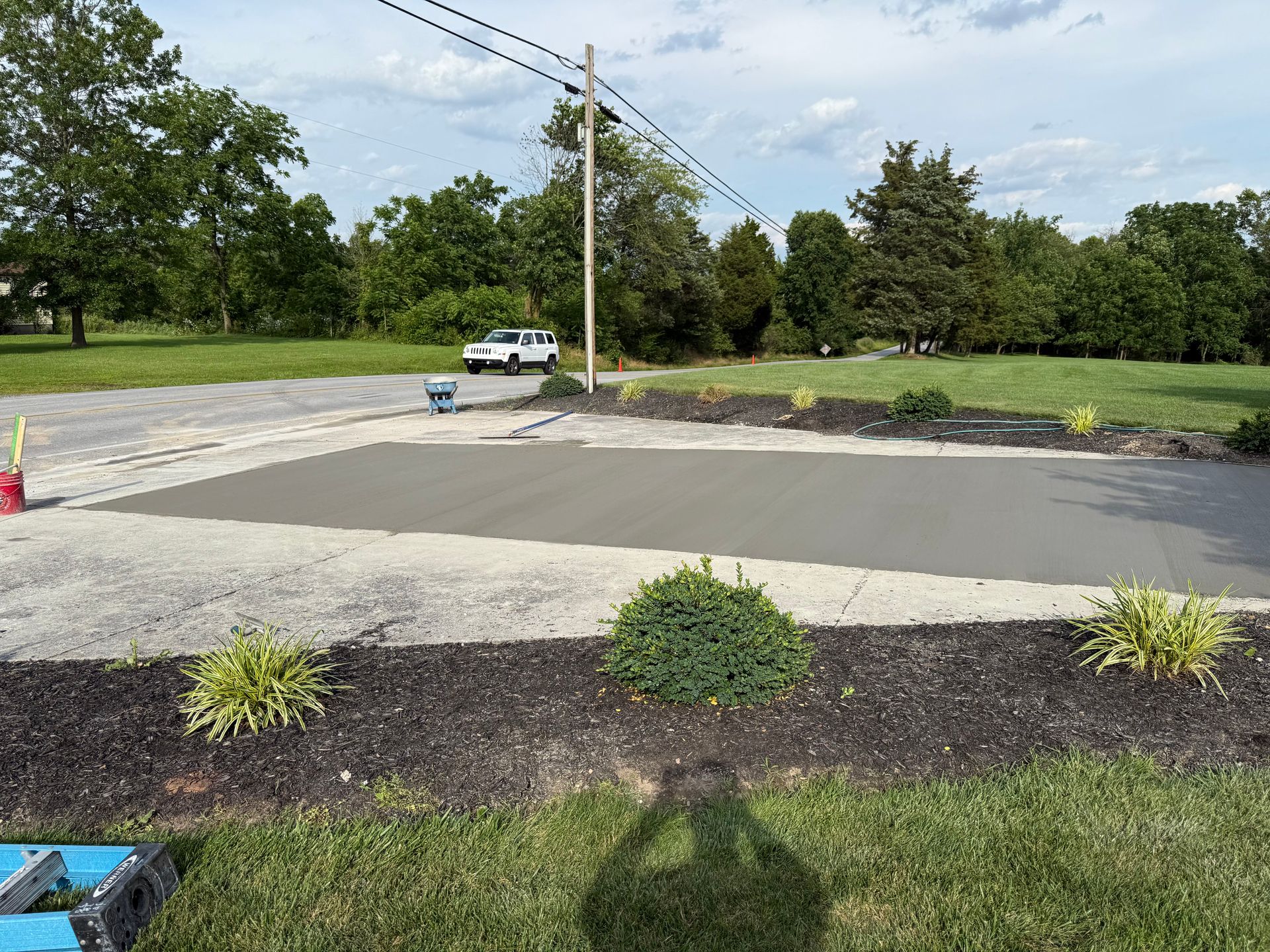 Freshly poured concrete driveway section with landscaping and vehicle in the background.