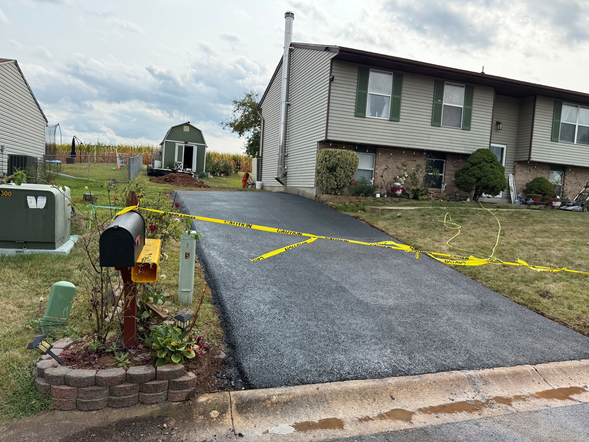 Newly paved driveway with yellow caution tape, next to a townhouse and mailbox.