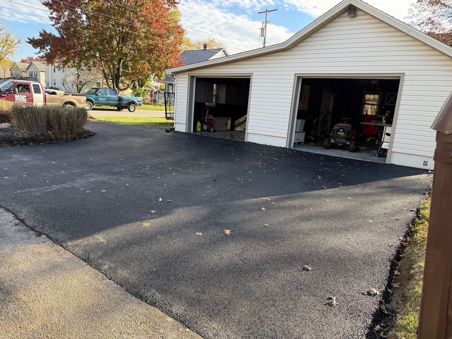 Newly paved asphalt driveway leading to a two-car garage with open doors.