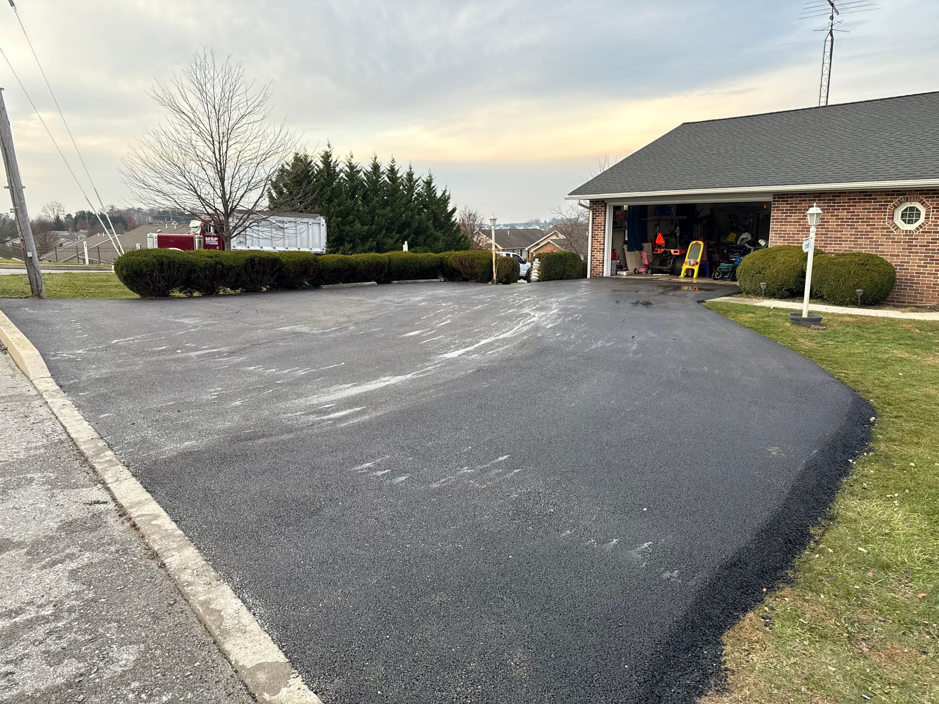 Newly paved asphalt driveway leading to a brick garage.