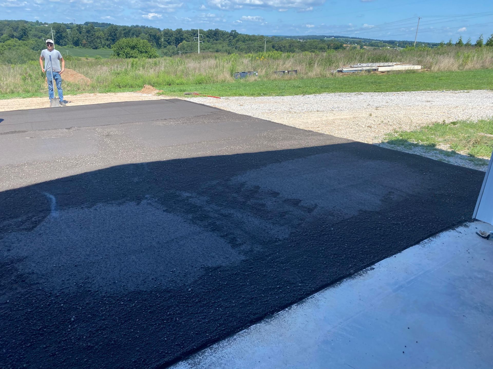 A newly paved asphalt driveway with a person standing nearby in a rural setting.