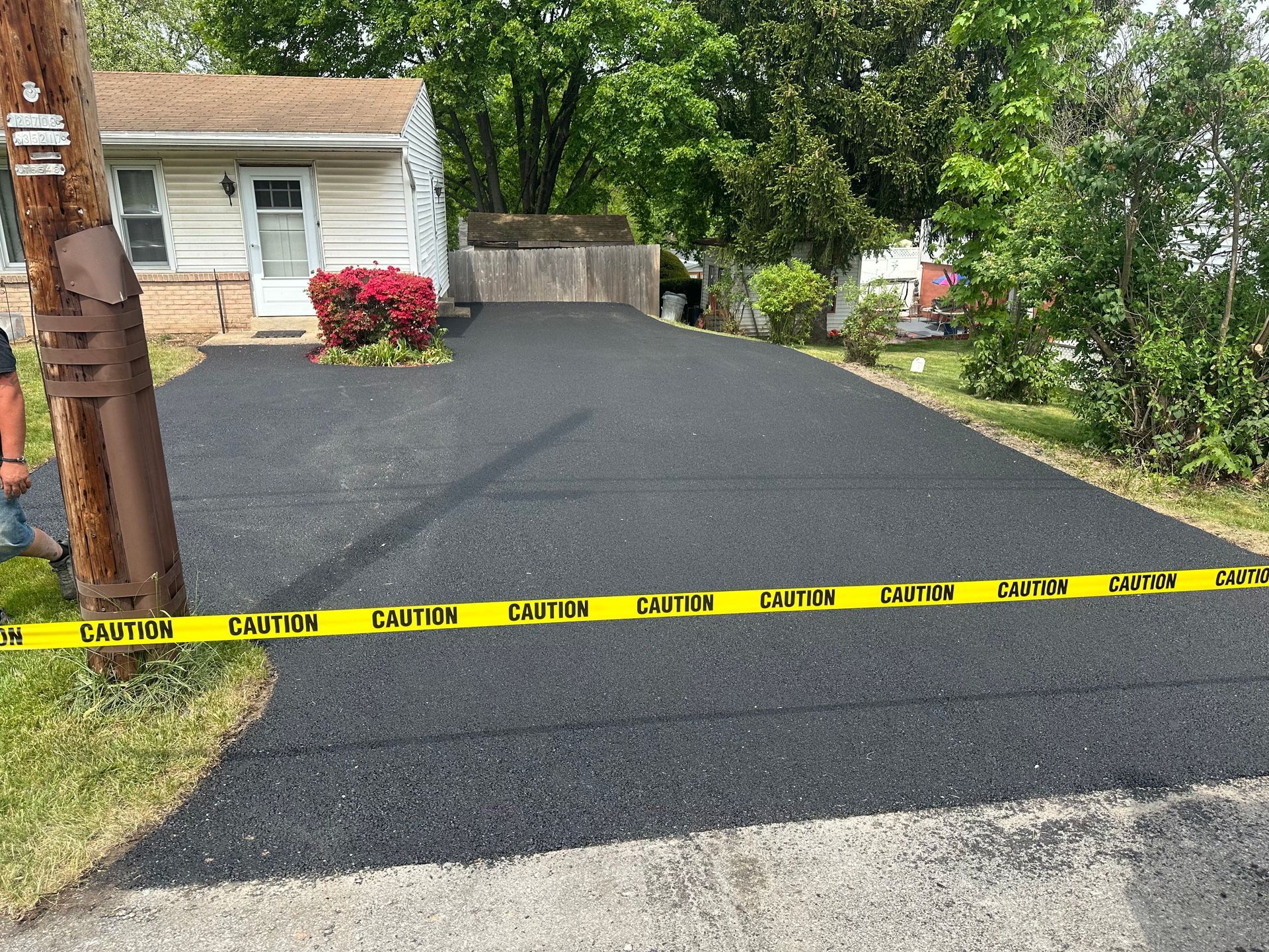 Freshly paved asphalt driveway with caution tape in front of a house.