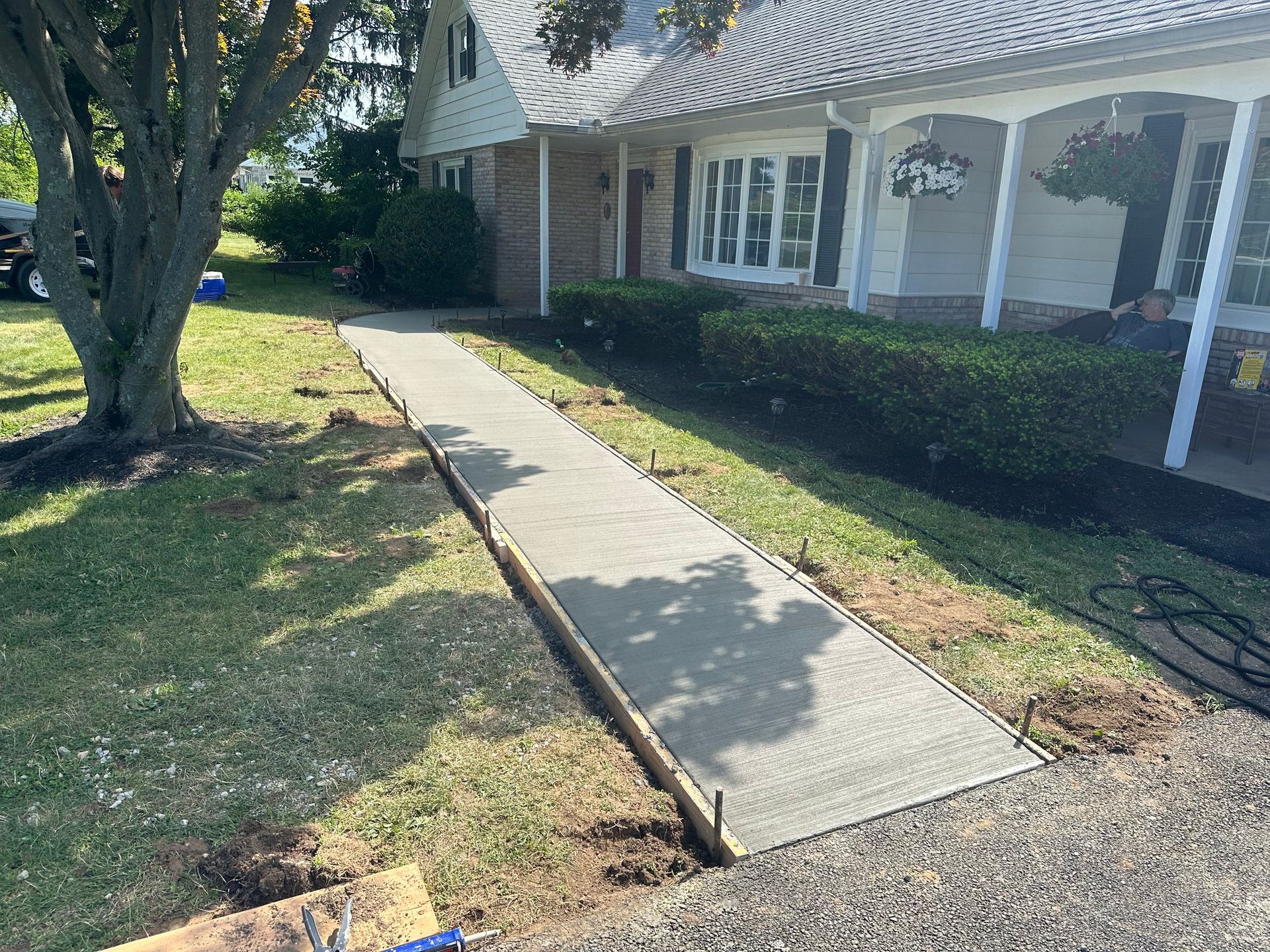 Freshly poured concrete sidewalk leading to a white house with a porch, surrounded by grass.