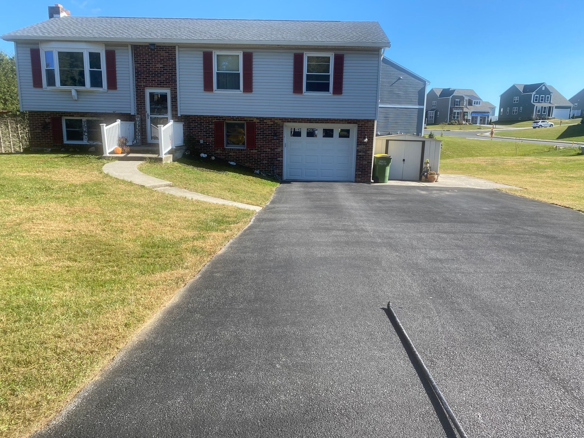 A two-story house with a driveway. Red brick base, gray siding, and a white garage door. Green lawn.