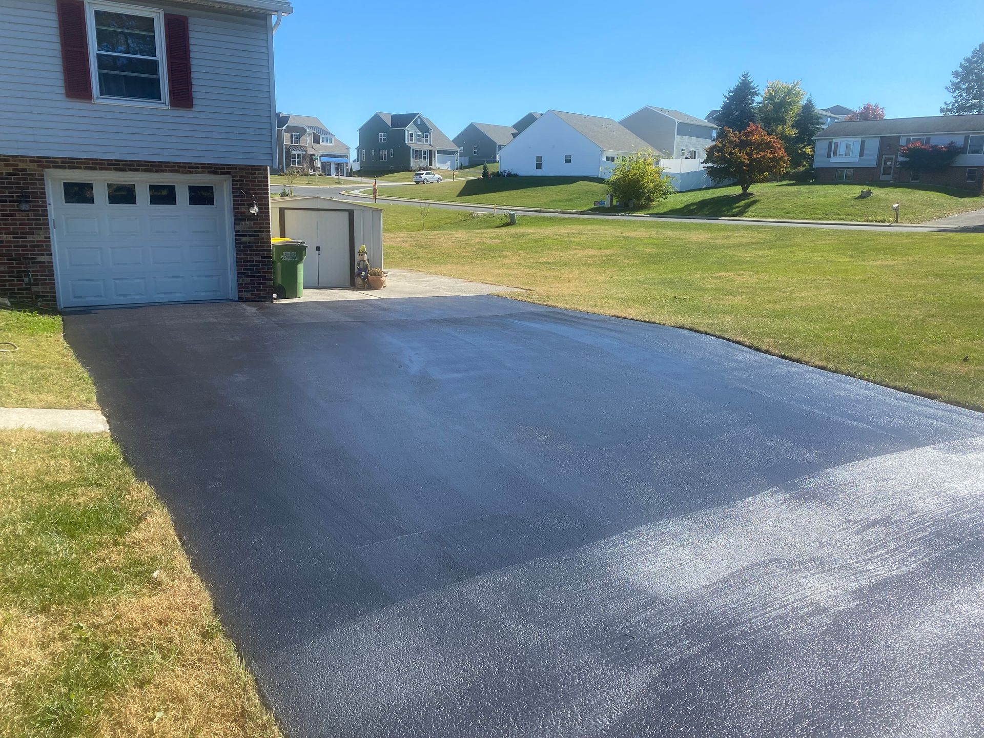 Black asphalt driveway in front of a house, green grass, and blue sky.