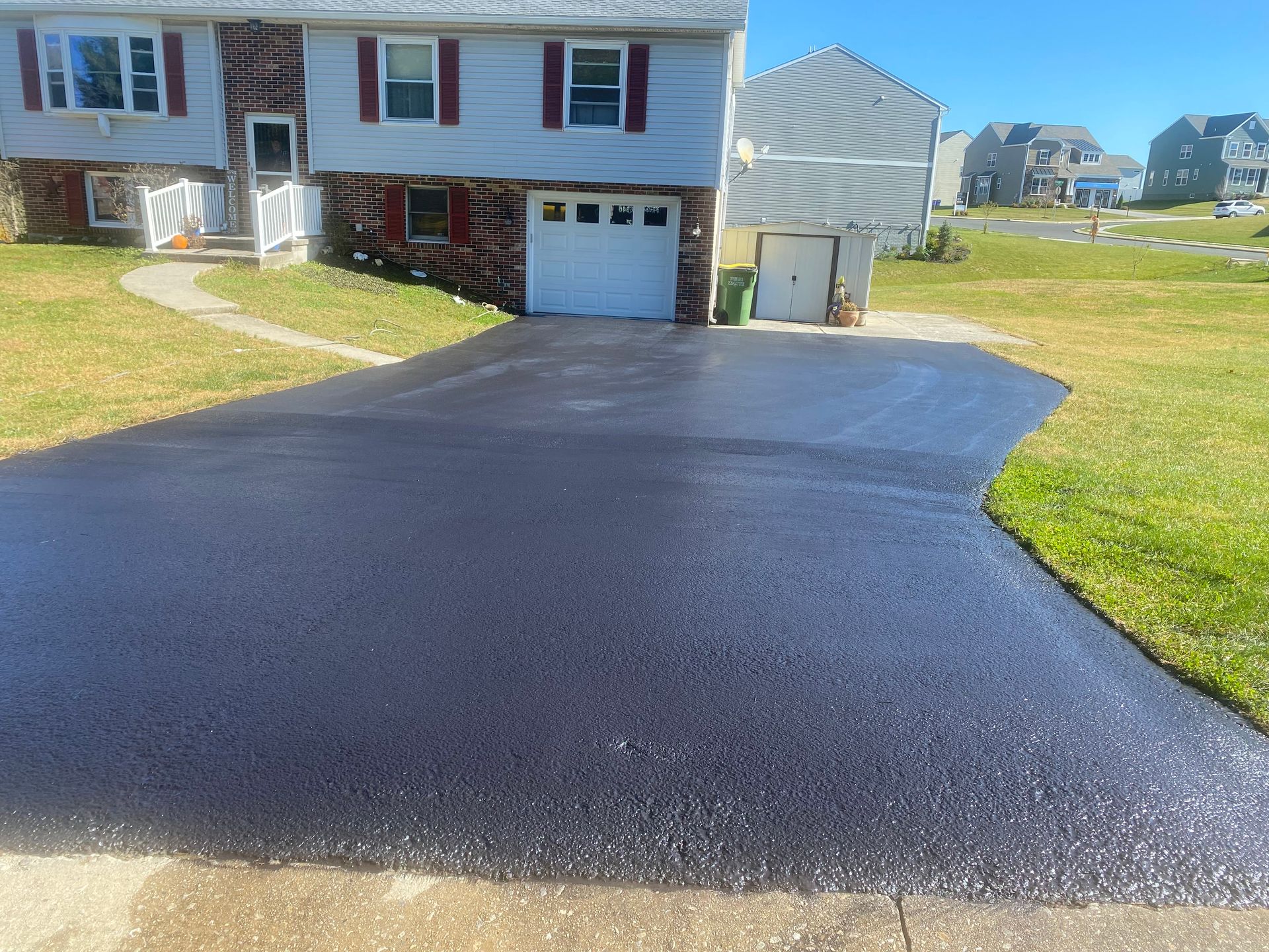 Freshly paved asphalt driveway in front of a light blue house with red shutters.