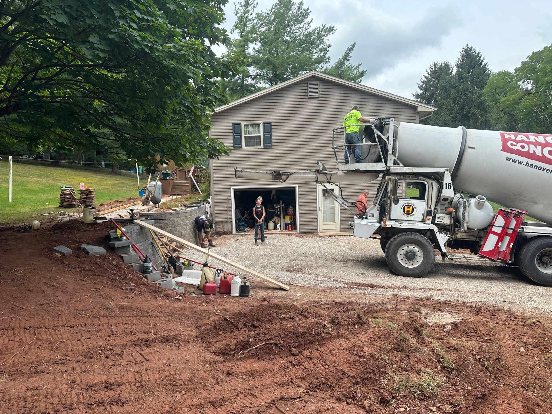 Concrete truck pouring concrete near a house, construction workers present.