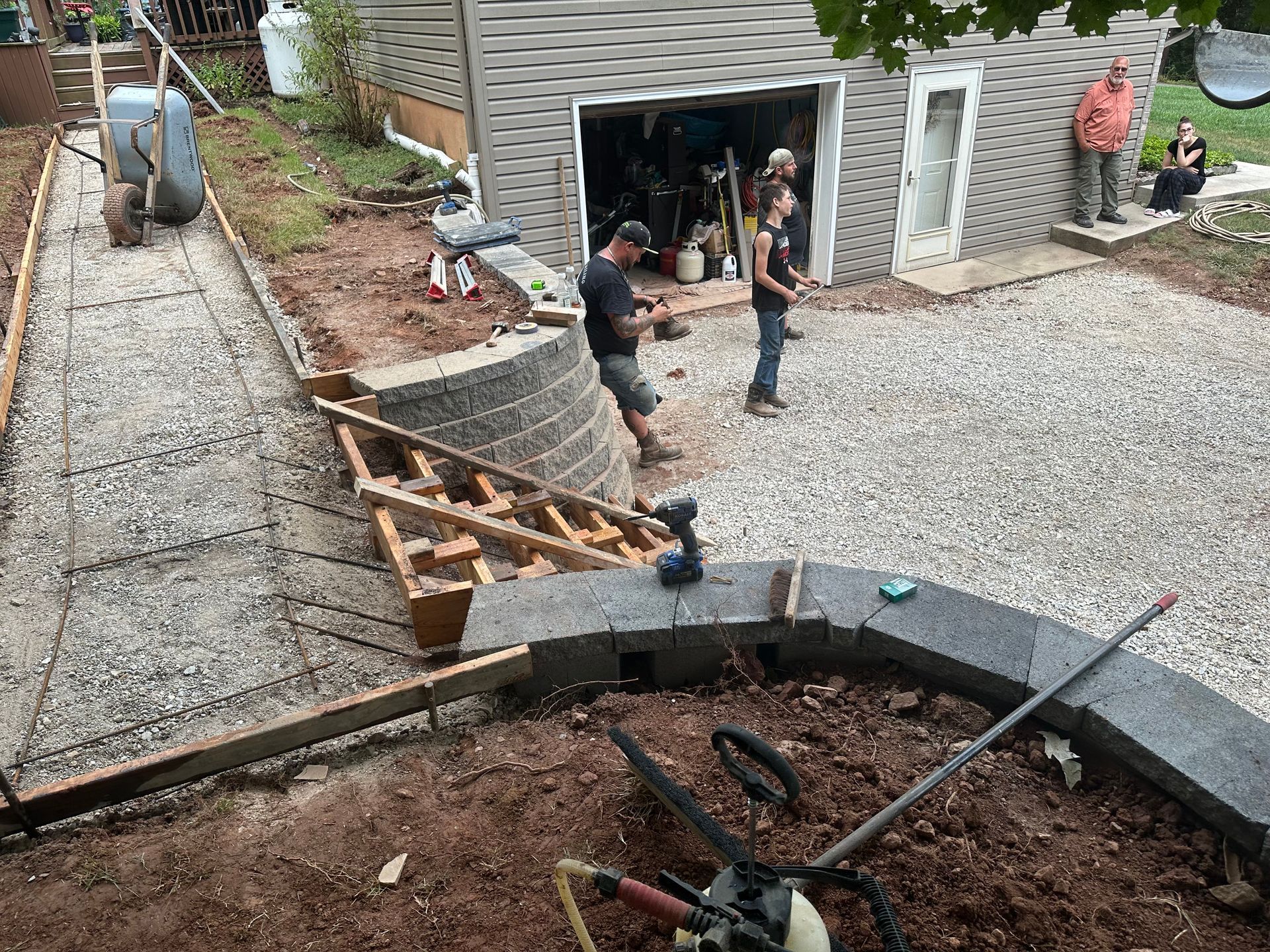 Workers building a retaining wall and walkway with gravel and blocks near a garage.