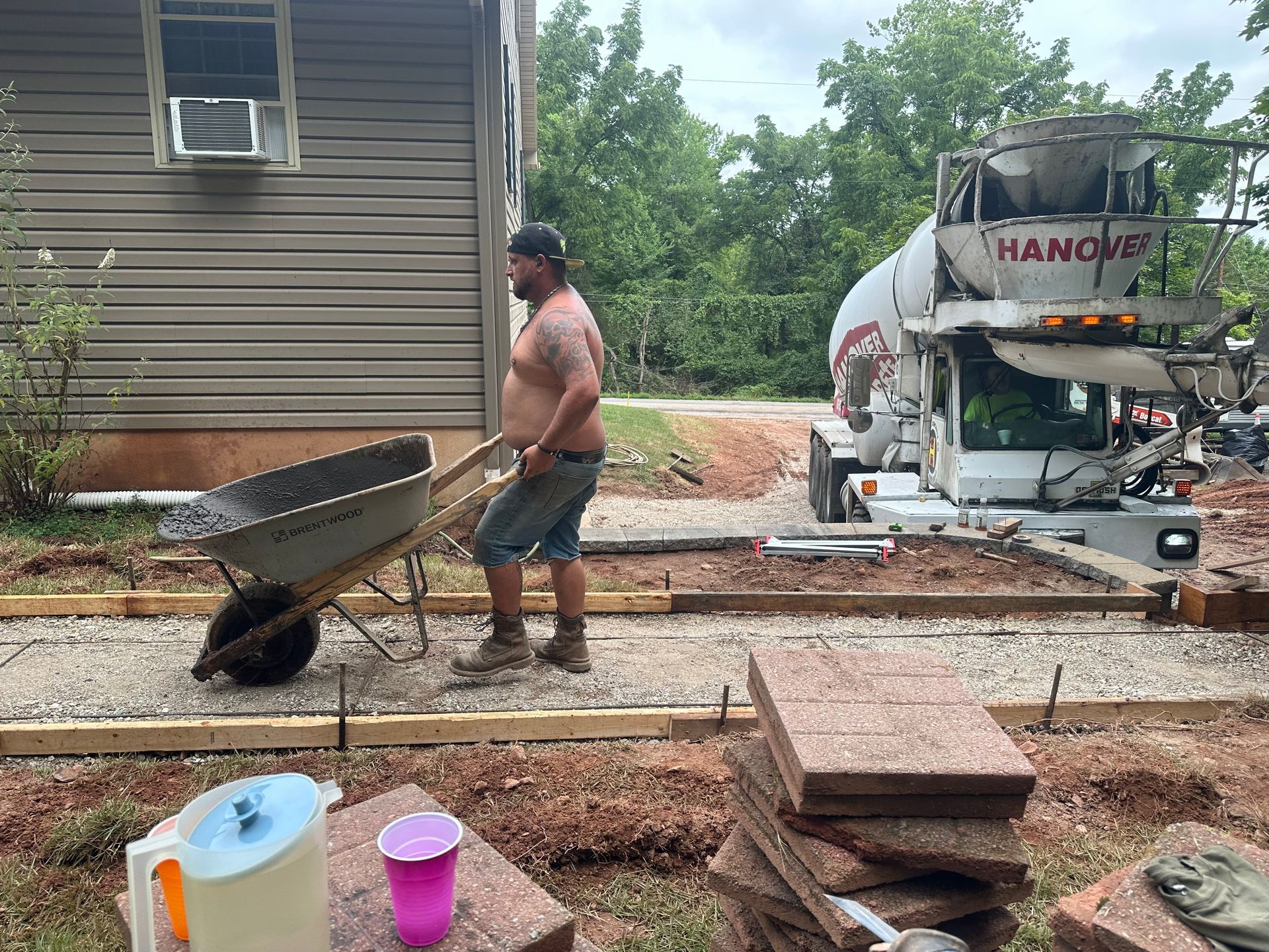 Man pushing a wheelbarrow on a construction site next to a concrete truck.