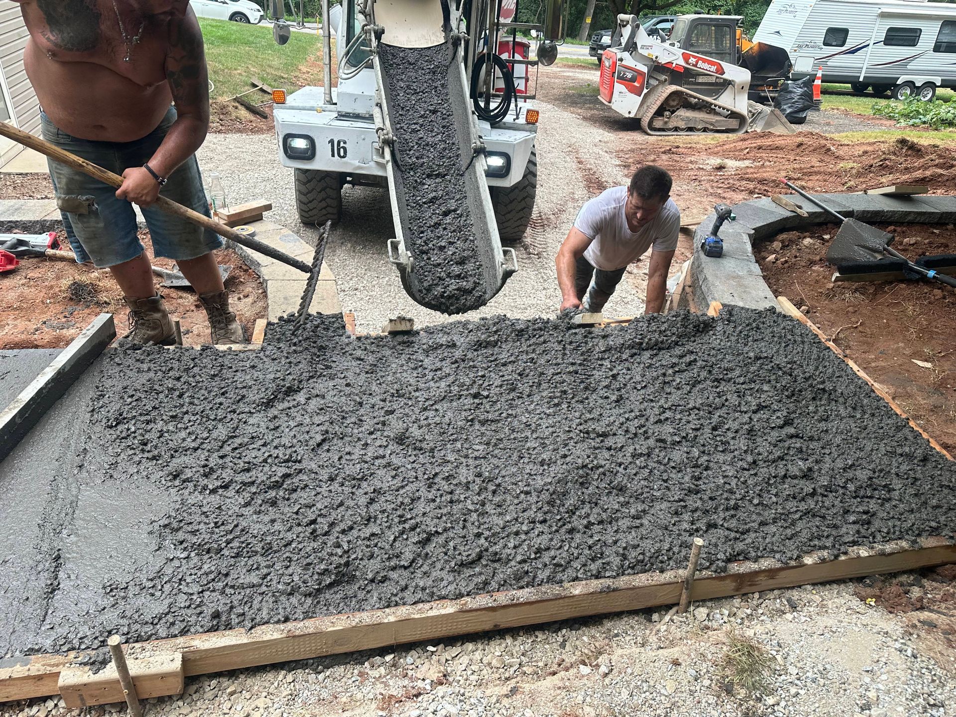 Men pouring concrete into wooden forms with a cement truck, outdoor setting.
