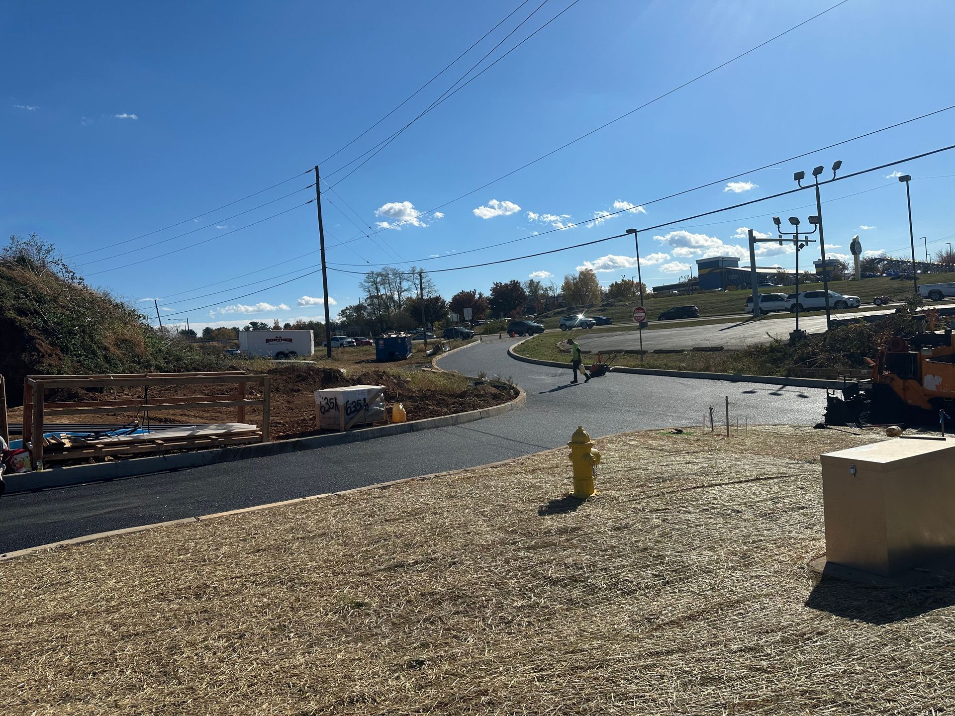 New asphalt road under construction, with a yellow fire hydrant and gravel ground cover. Sunny, outdoor setting.