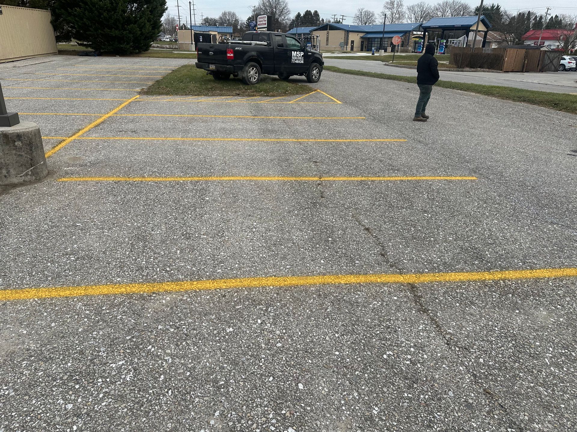 Gravel parking lot with yellow lines, a parked black truck, and a person standing nearby.