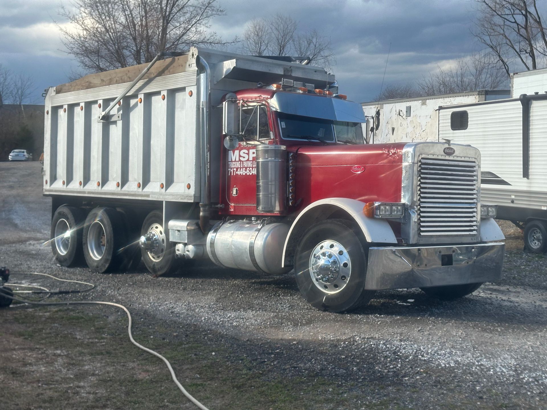 Red and silver dump truck being washed outdoors. 