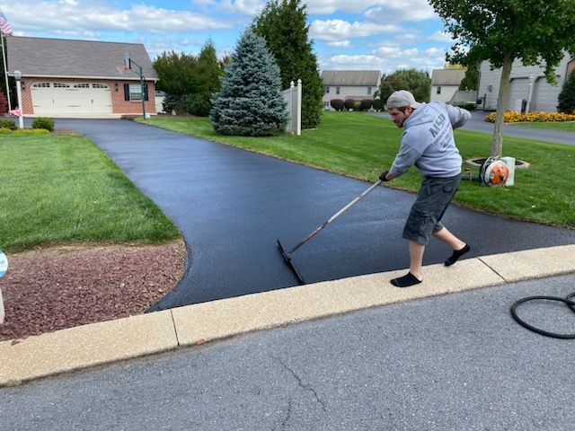 A man is painting a driveway with a rake.