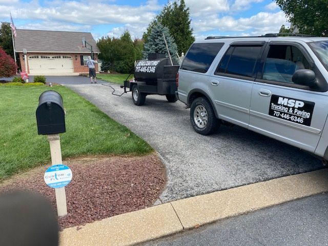 A silver suv is parked in front of a house with a trailer attached to it.