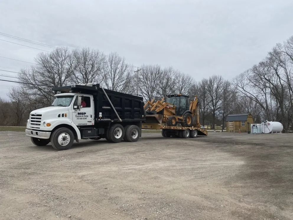 A dump truck is towing a tractor in a parking lot.