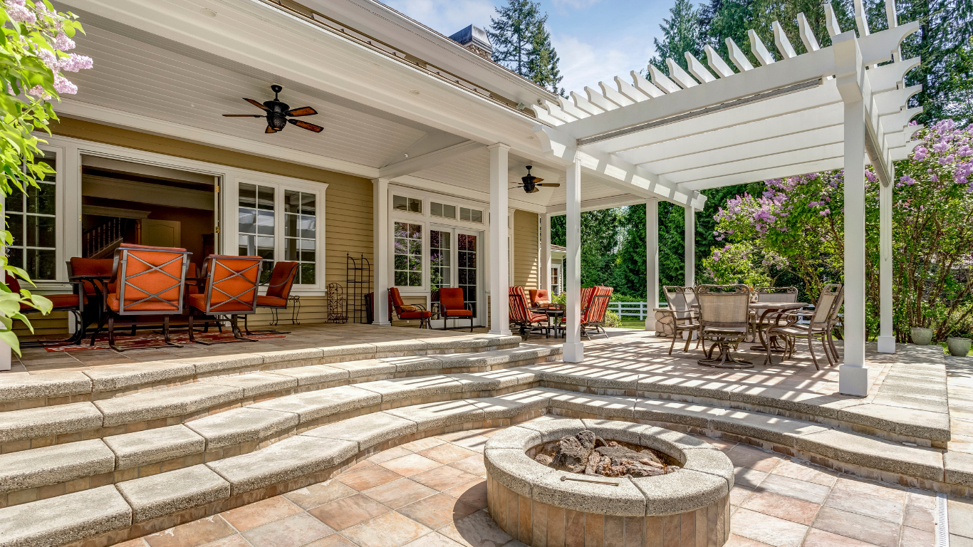 Back patio with stone steps, a circular fire pit, outdoor seating under a covered porch, and a white pergola area.
