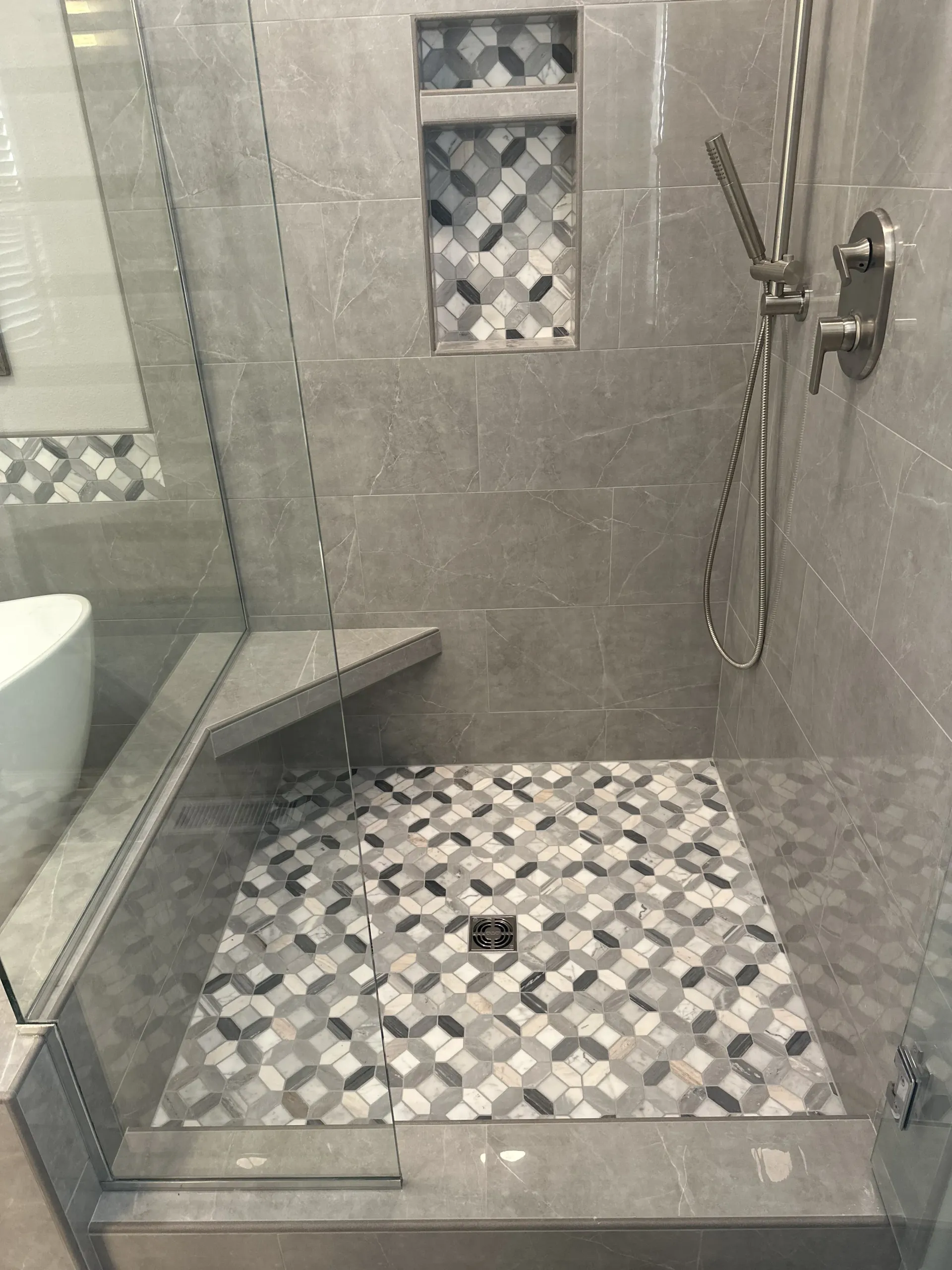 A walk-in shower with gray stone walls, a built-in bench, a patterned tile floor, and a matching recessed wall niche.