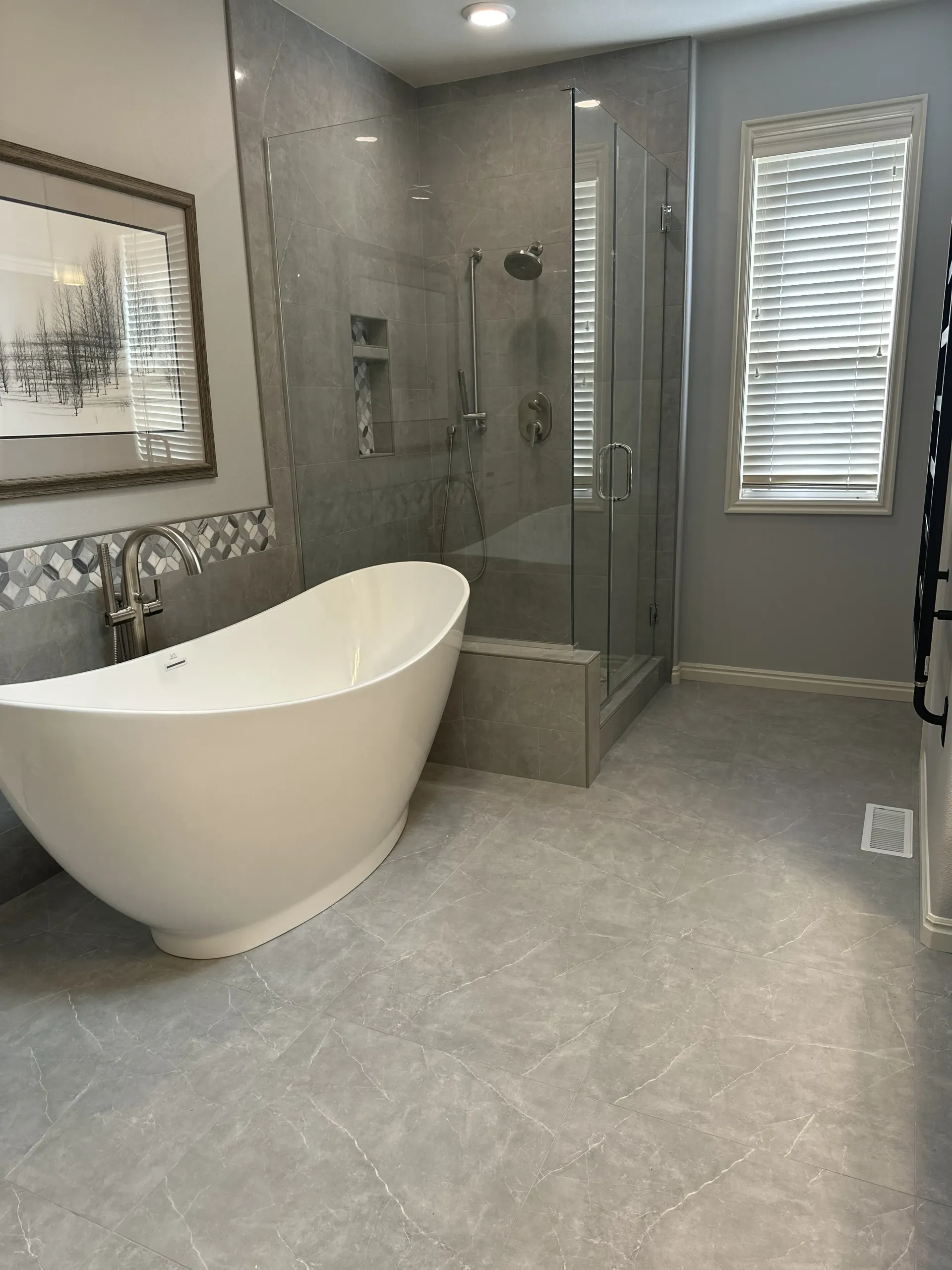 Modern bathroom with a freestanding white oval bathtub next to a glass-enclosed walk-in shower on gray tiled flooring.