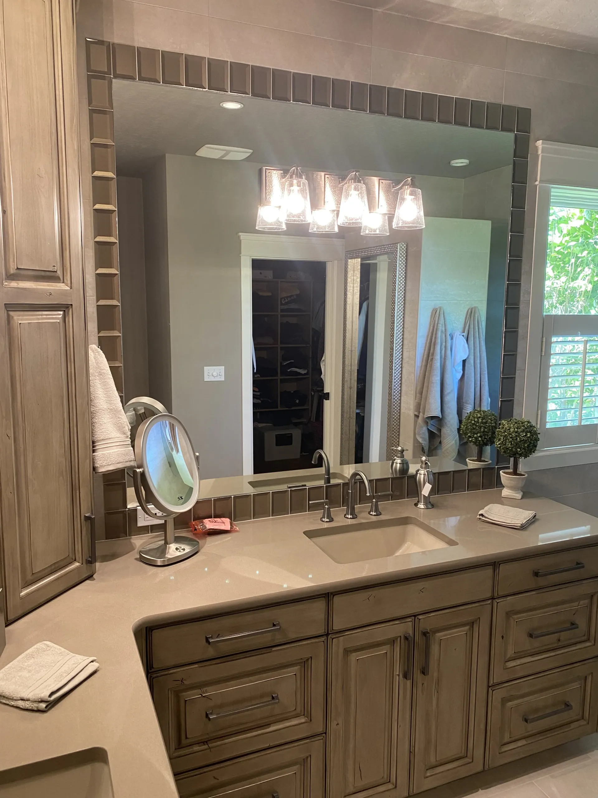 A bathroom vanity with a large mirror framed in wood tiles, neutral stone countertops, and rustic wooden cabinets.