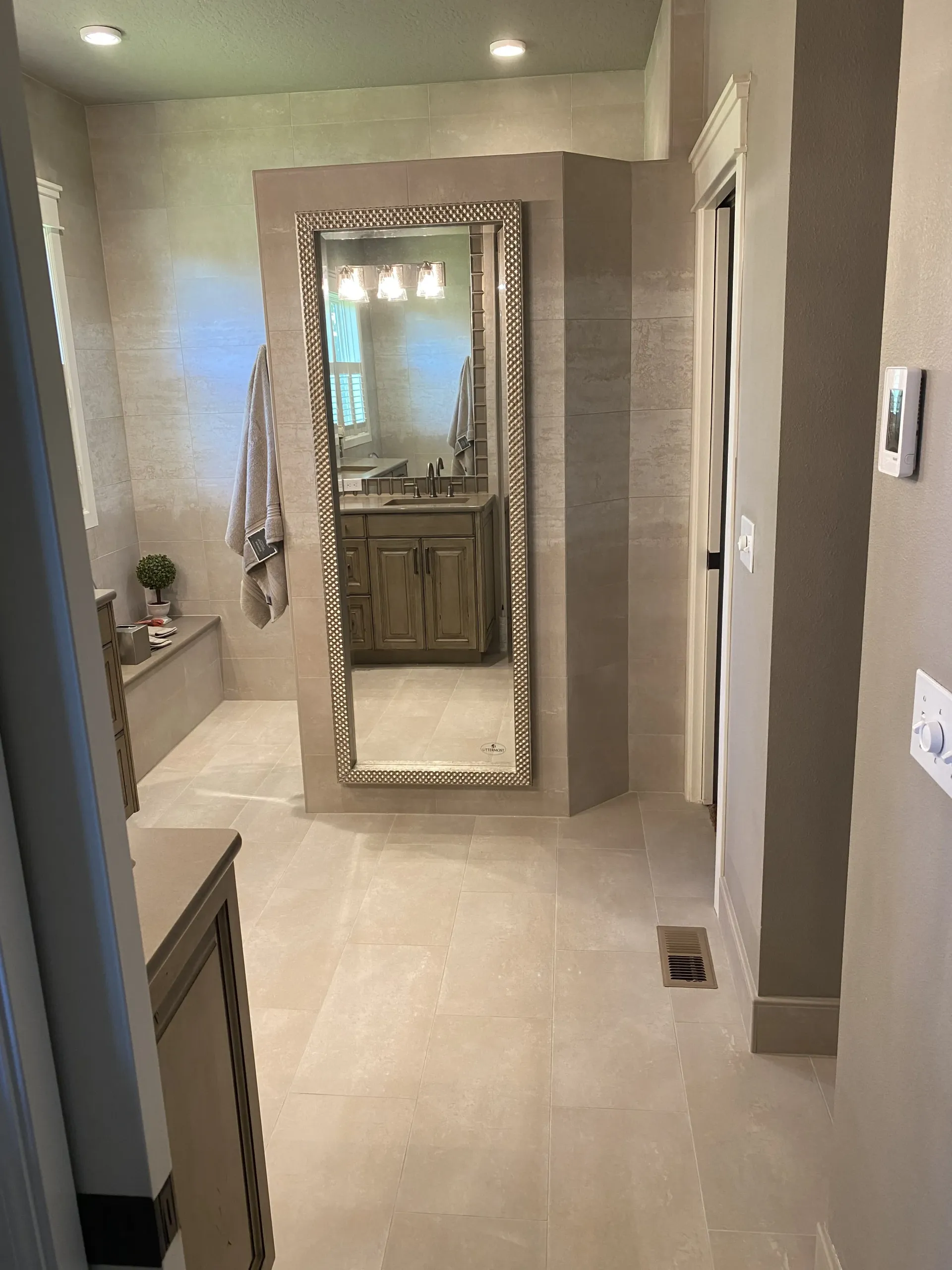 A view of a modern bathroom with neutral-toned tiled walls and floors, featuring a large mirror and recessed lighting.