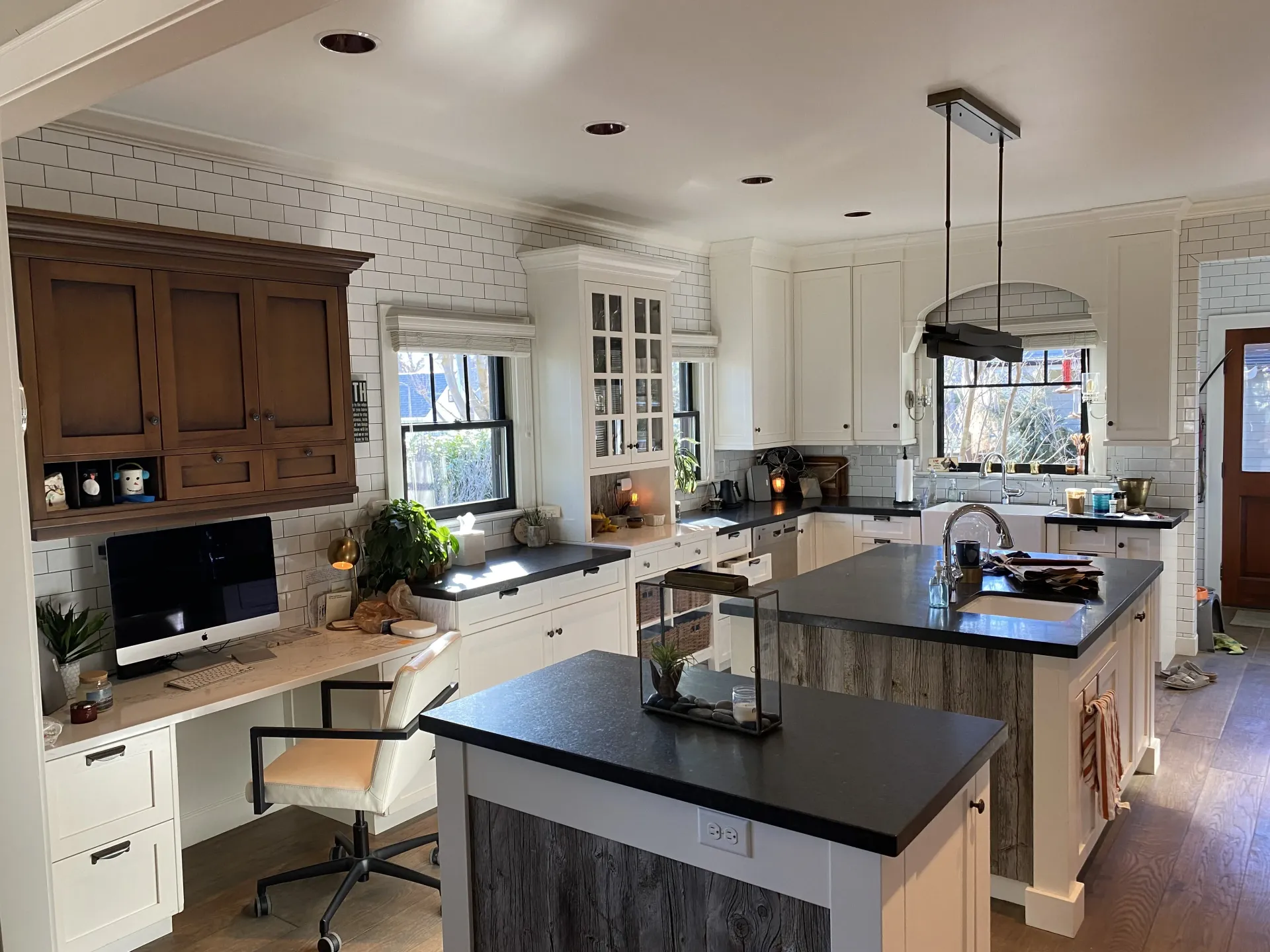 Kitchen featuring two islands with black countertops, a workspace with a computer, white cabinets, and spotted wallpaper.