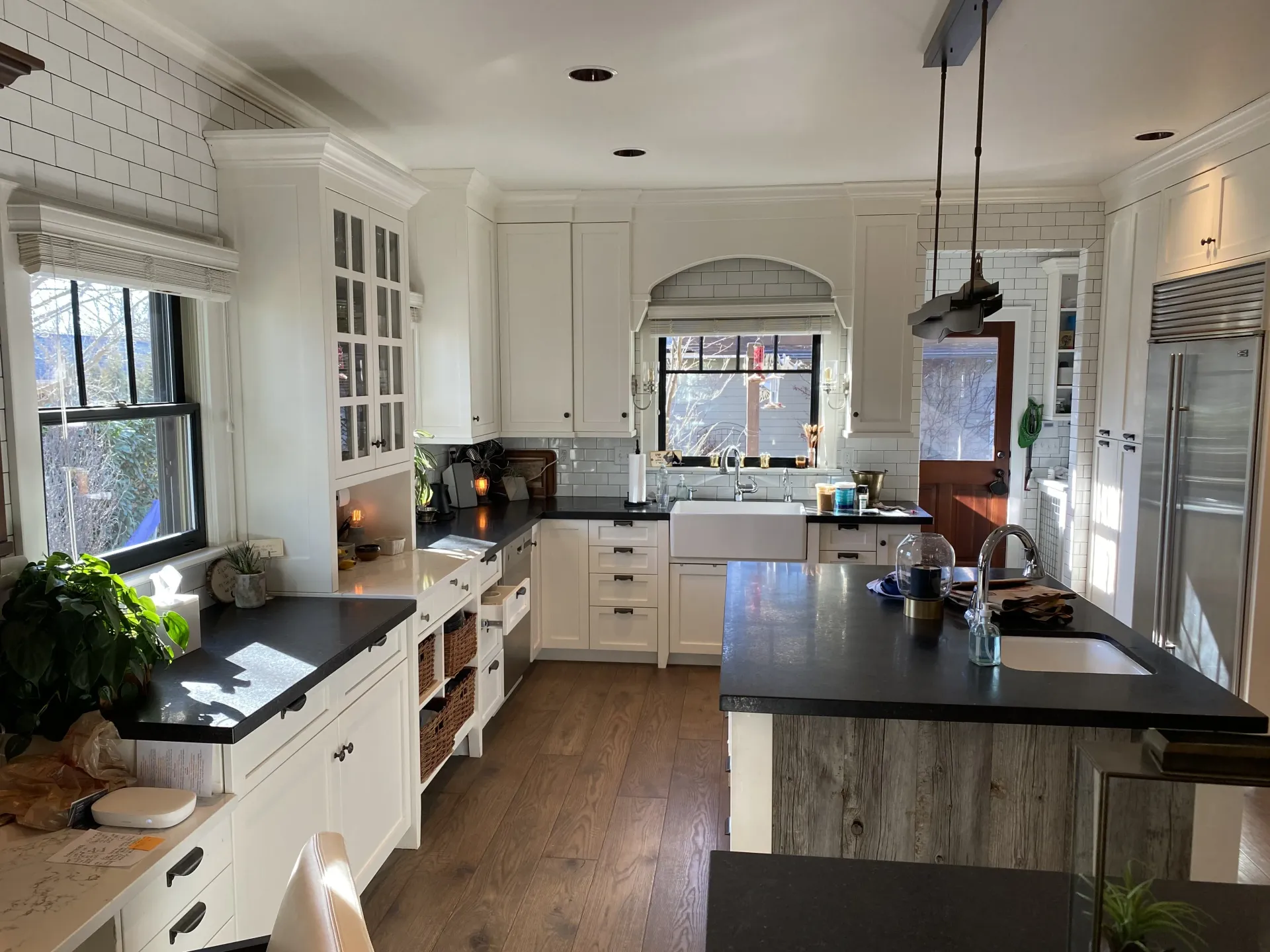 A bright, modern kitchen featuring white cabinets, dark countertops, an island, and hardwood floors.