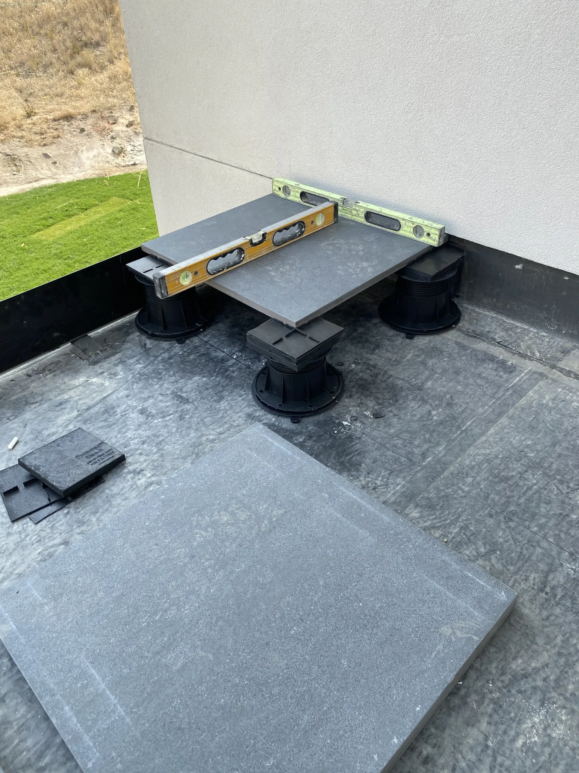 A grey paver tile on adjustable plastic pedestals on a roof, with a spirit level checking for a flat surface.