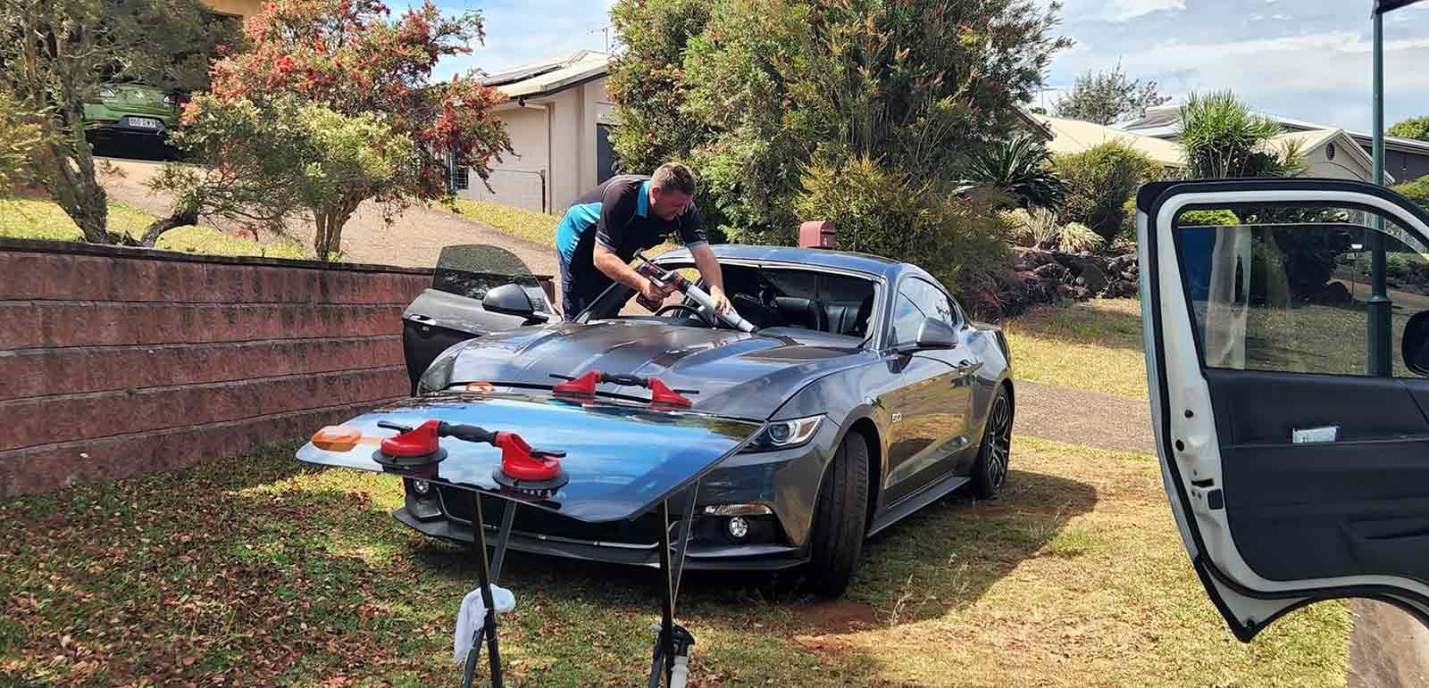 A Man is Installing a Windshield on a Car — FNQ Windscreens in Bungalow, QLD