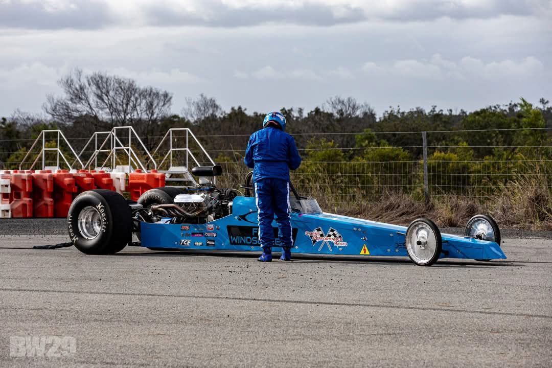 A Man is Standing Next to a Blue Dragster on a Track — FNQ Windscreens in Bungalow, QLD