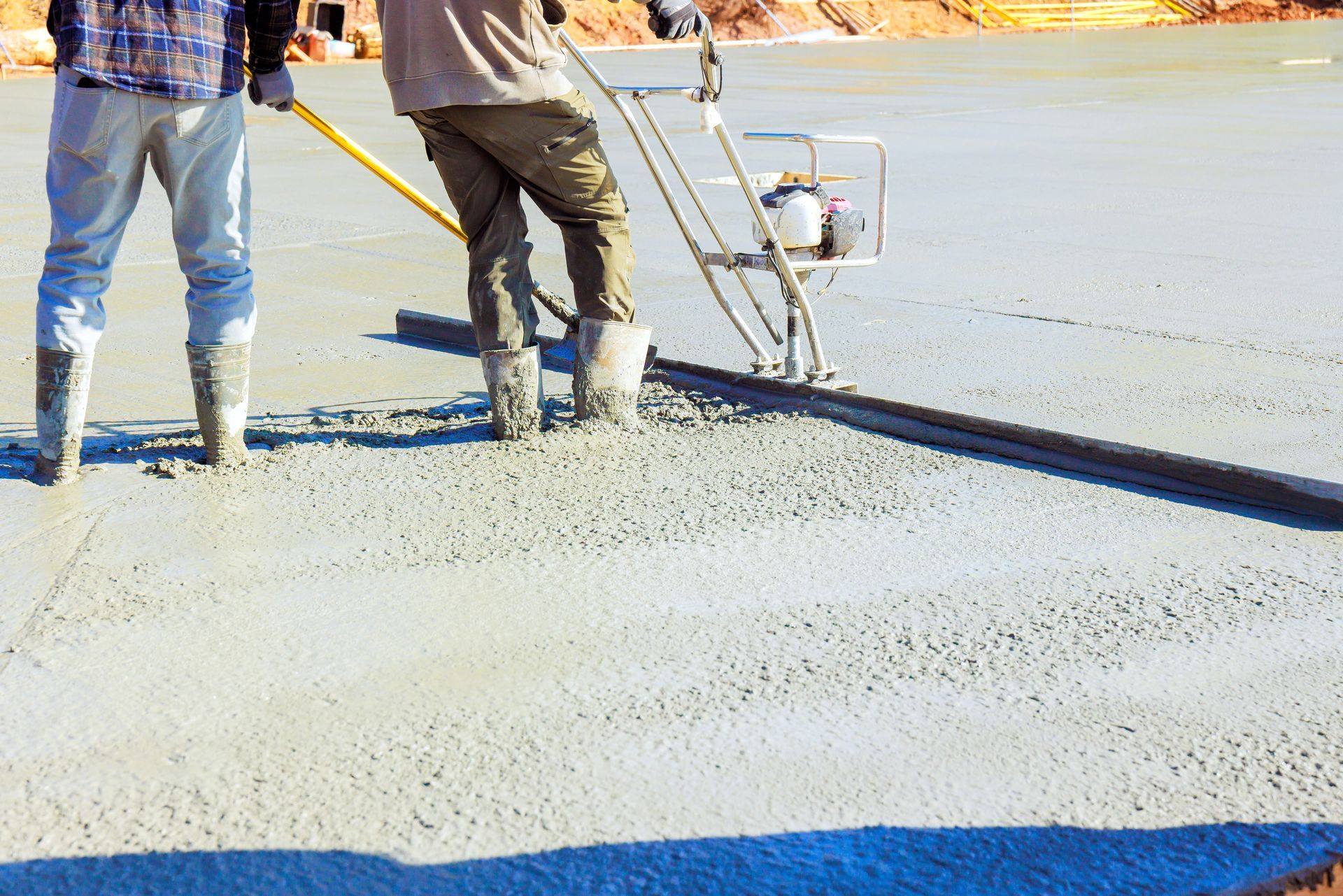 Two workers leveling wet concrete with a screed and a machine. Construction site.
