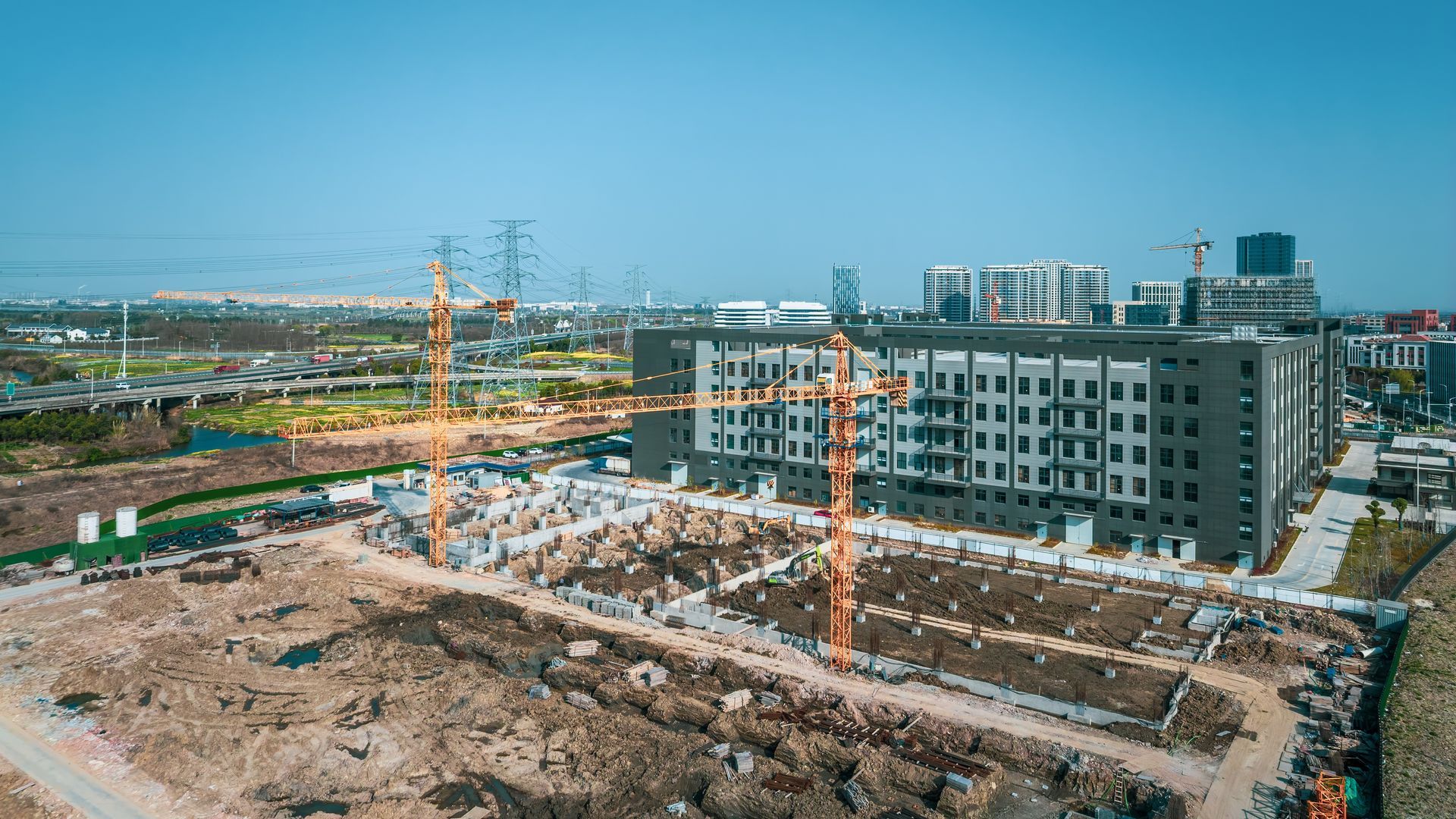 Construction site with cranes, a partially built gray building, and a blue sky.