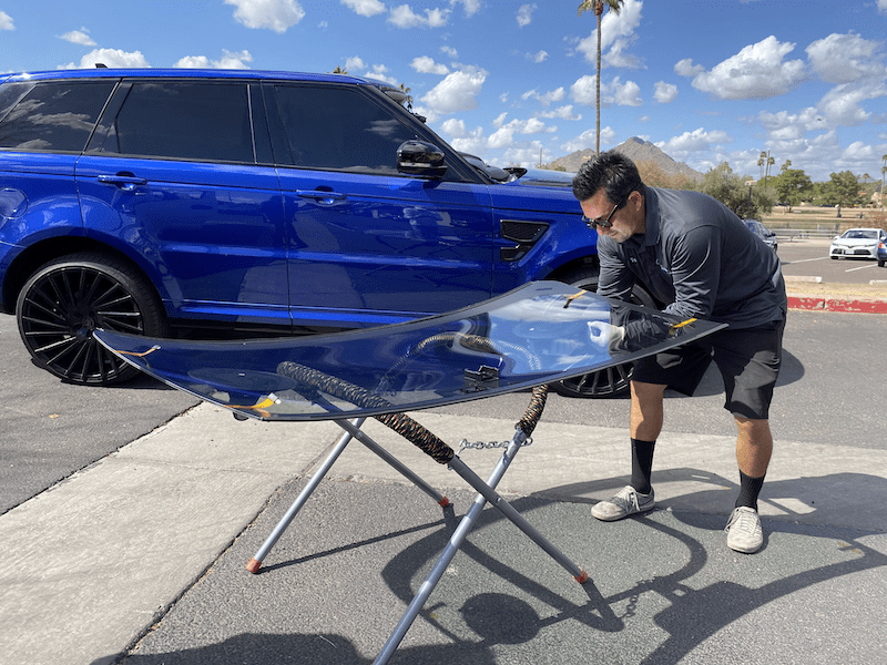 A man is working on a windshield in front of a blue range rover.