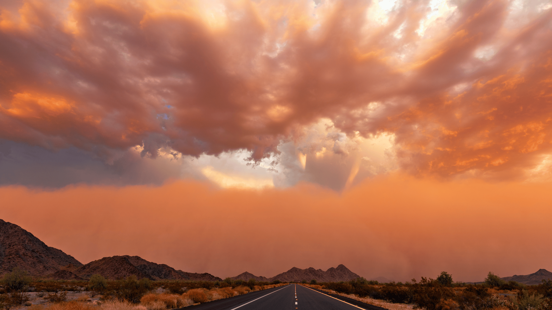 A road with a cloudy sky and mountains in the background at sunset.