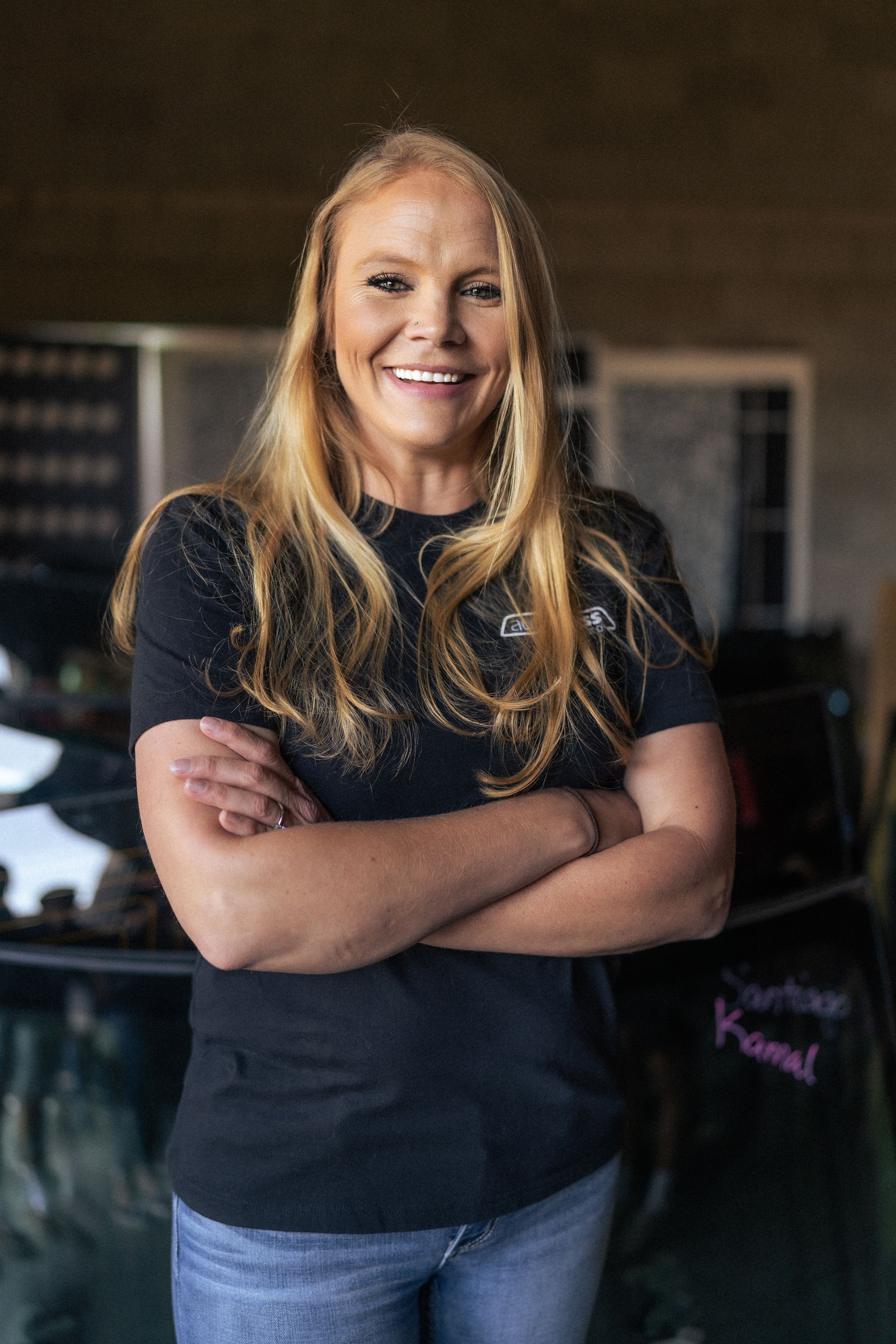 A woman is standing in front of a car with her arms crossed and smiling.