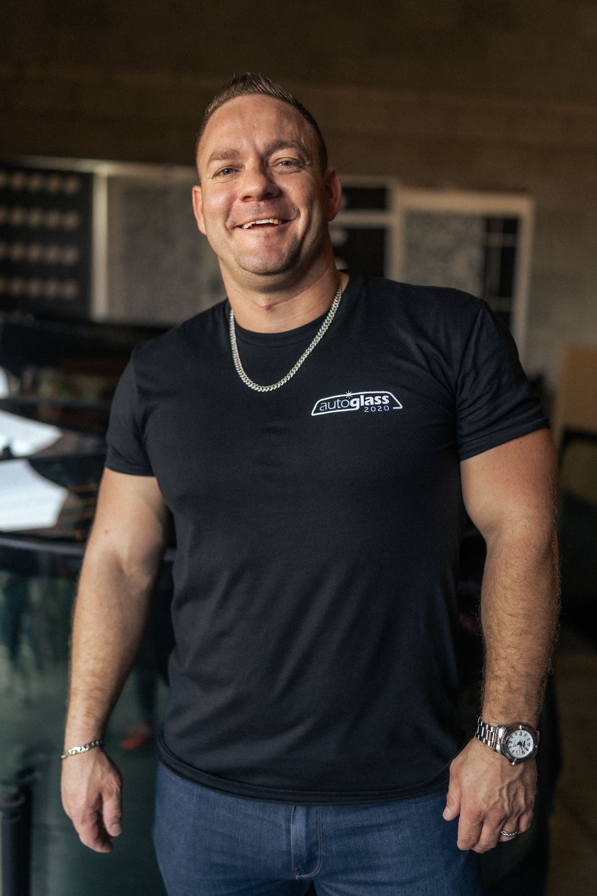 A man wearing a black t-shirt and a chain around his neck is smiling.