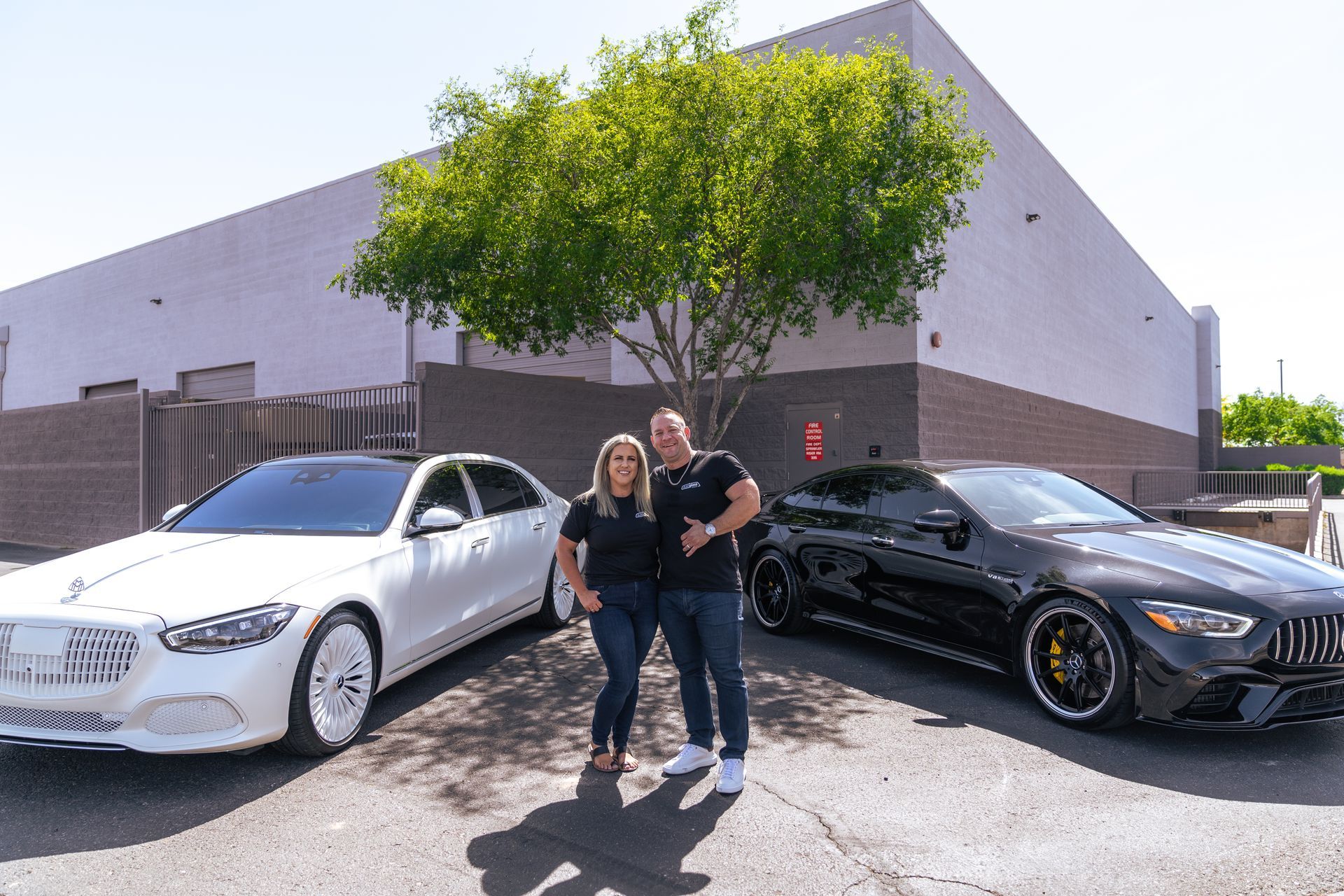 A man and a woman are standing in front of two cars.