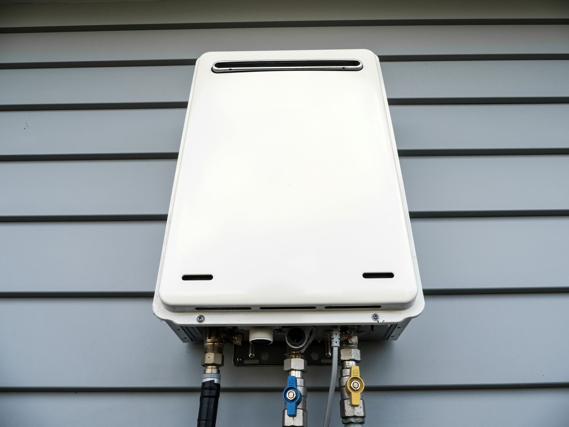 White wall-mounted tankless water heater with pipes and valves against gray siding