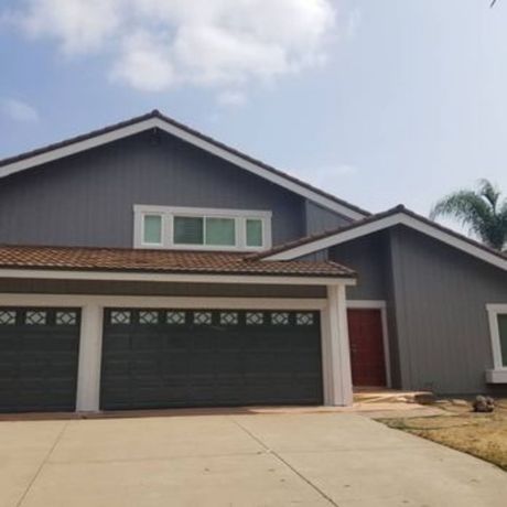 The right color - Gray house with brown roof, dark green garage doors, and red front door against a blue sky.