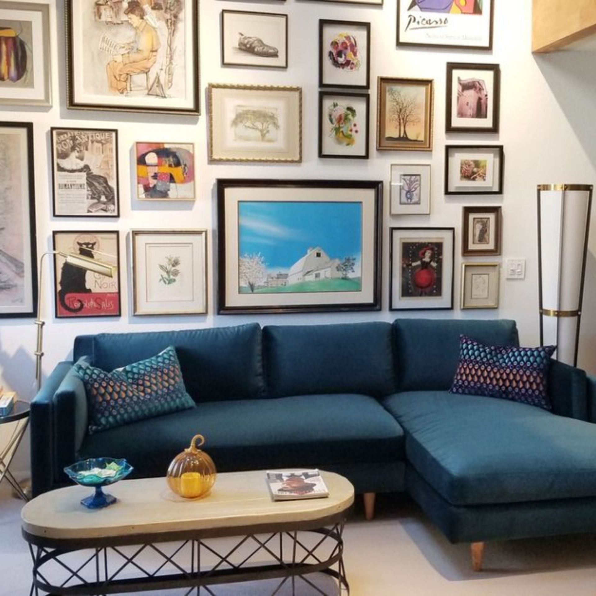 The right color - Teal sectional sofa under a gallery wall of framed art. Coffee table with decor. Tall floor lamp.