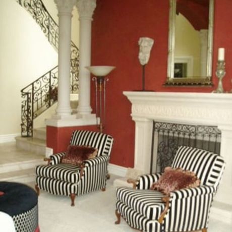 The right color - Living room with red wall, fireplace, striped chairs, staircase and marble columns.